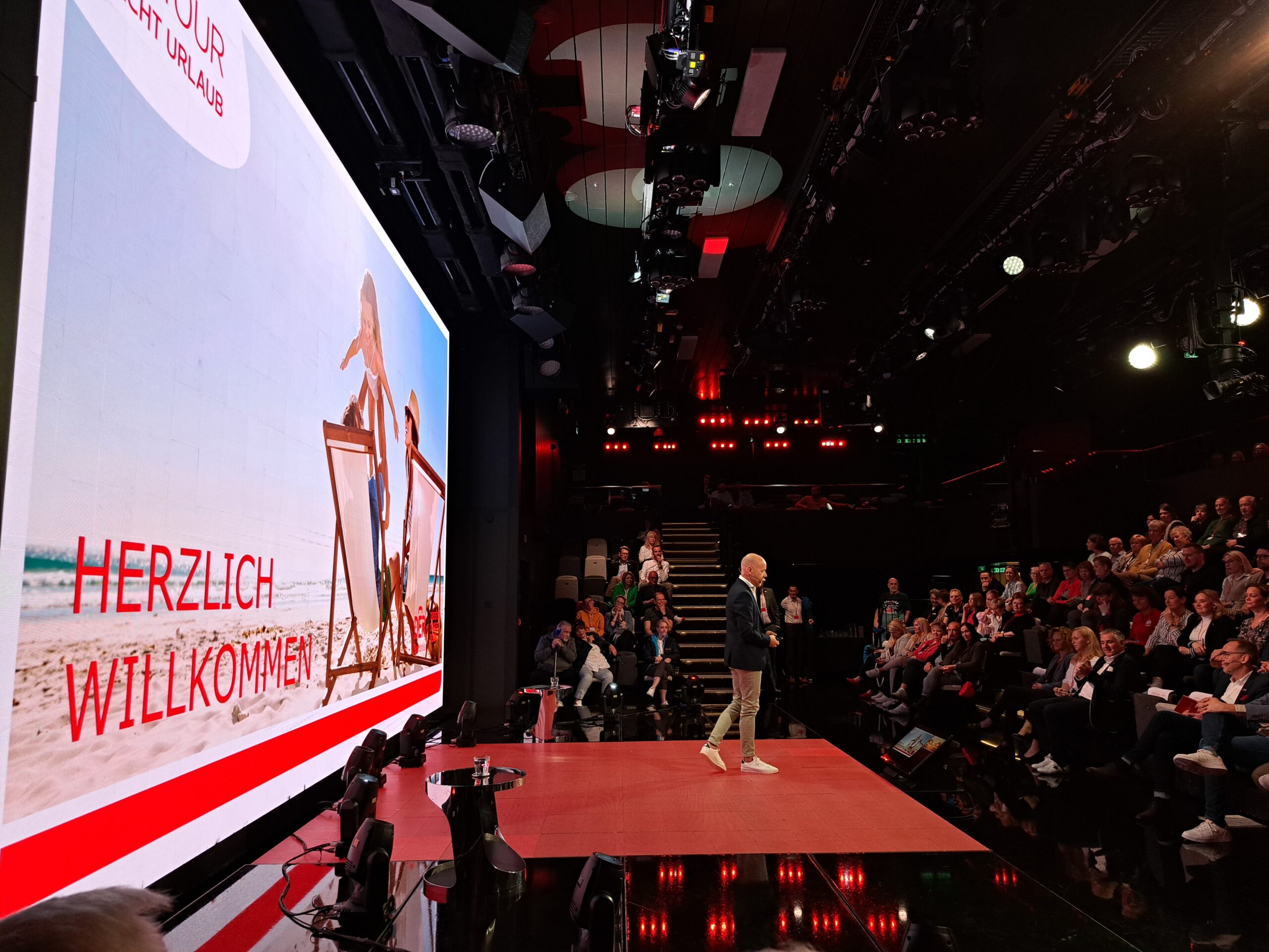 a man on a stage with a large screen and people watching