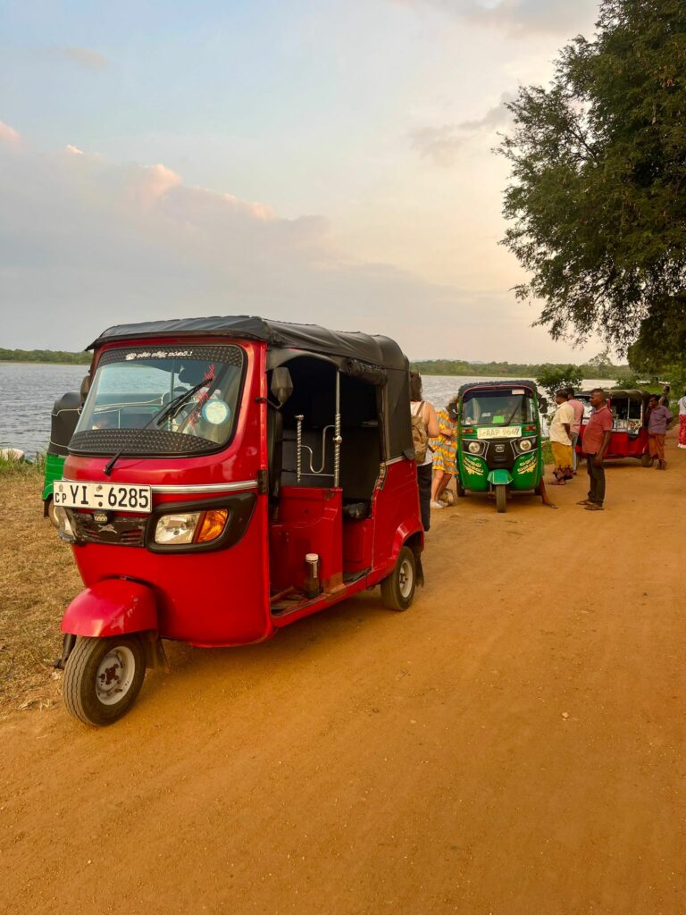 a group of people standing on a dirt road next to a red vehicle